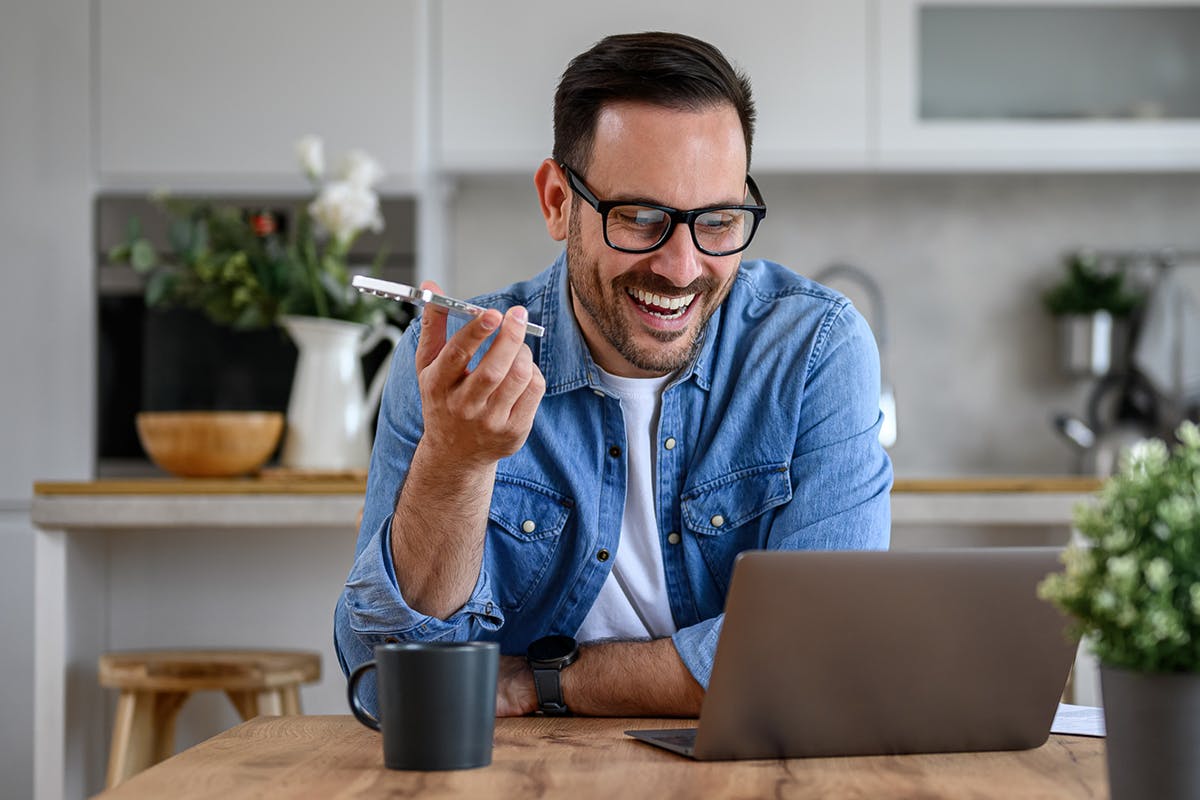 Smiling man taking a phone call while looking at his laptop.