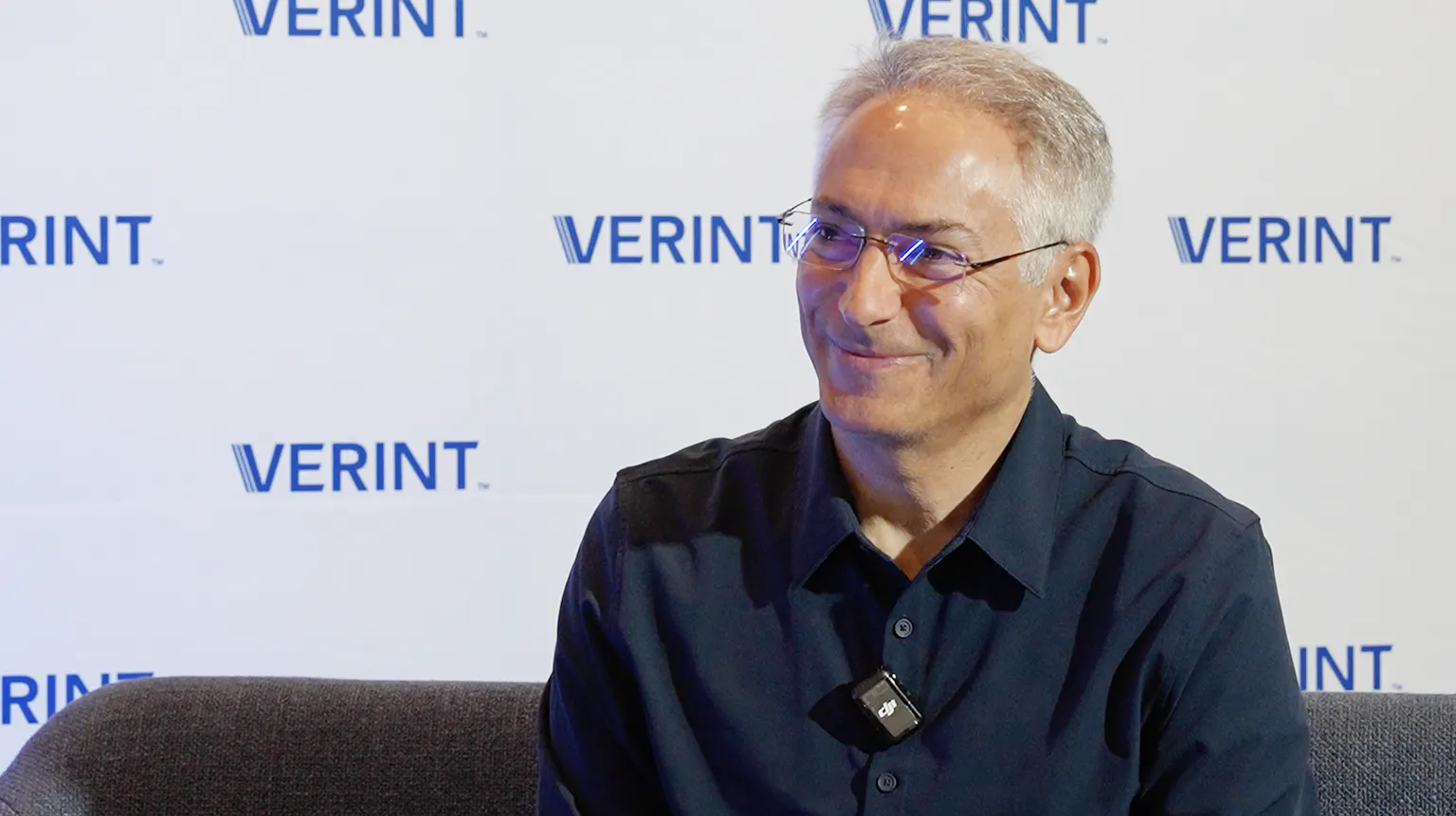 Daniel Ziv, GVP of AI and Analytics, sitting in front of a Verint-branded backdrop, explaining the importance of leveraging proprietary contact center interaction data.