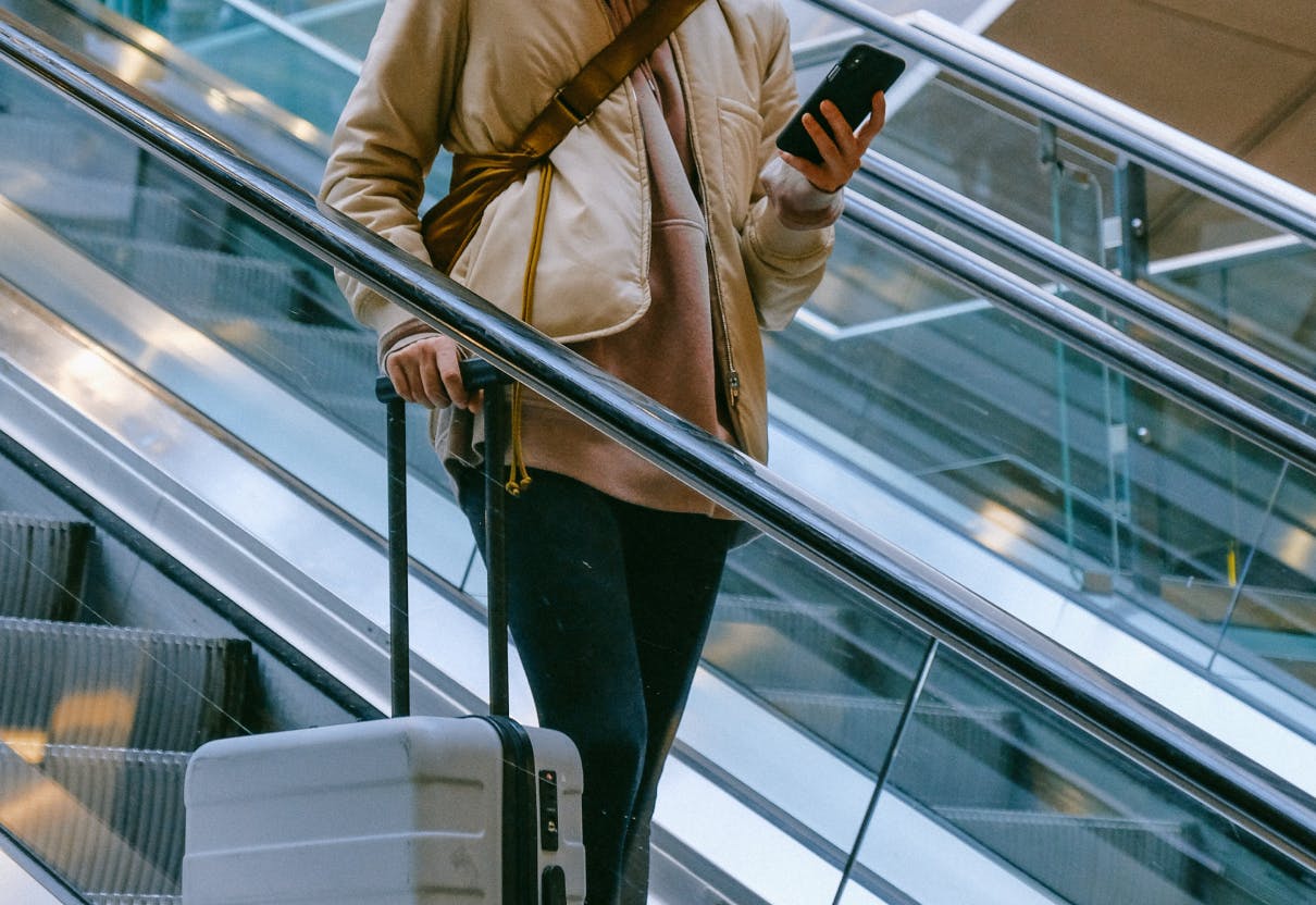 traveler with luggage going down escalators while using phone