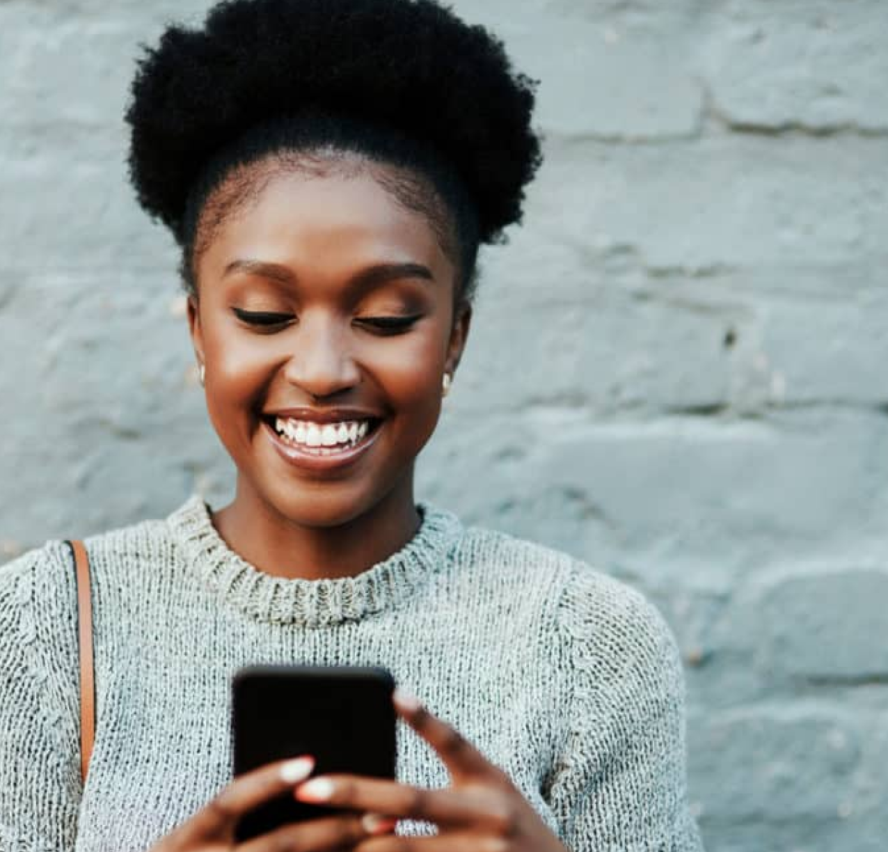 woman standing by brick wall holding phone and smiling