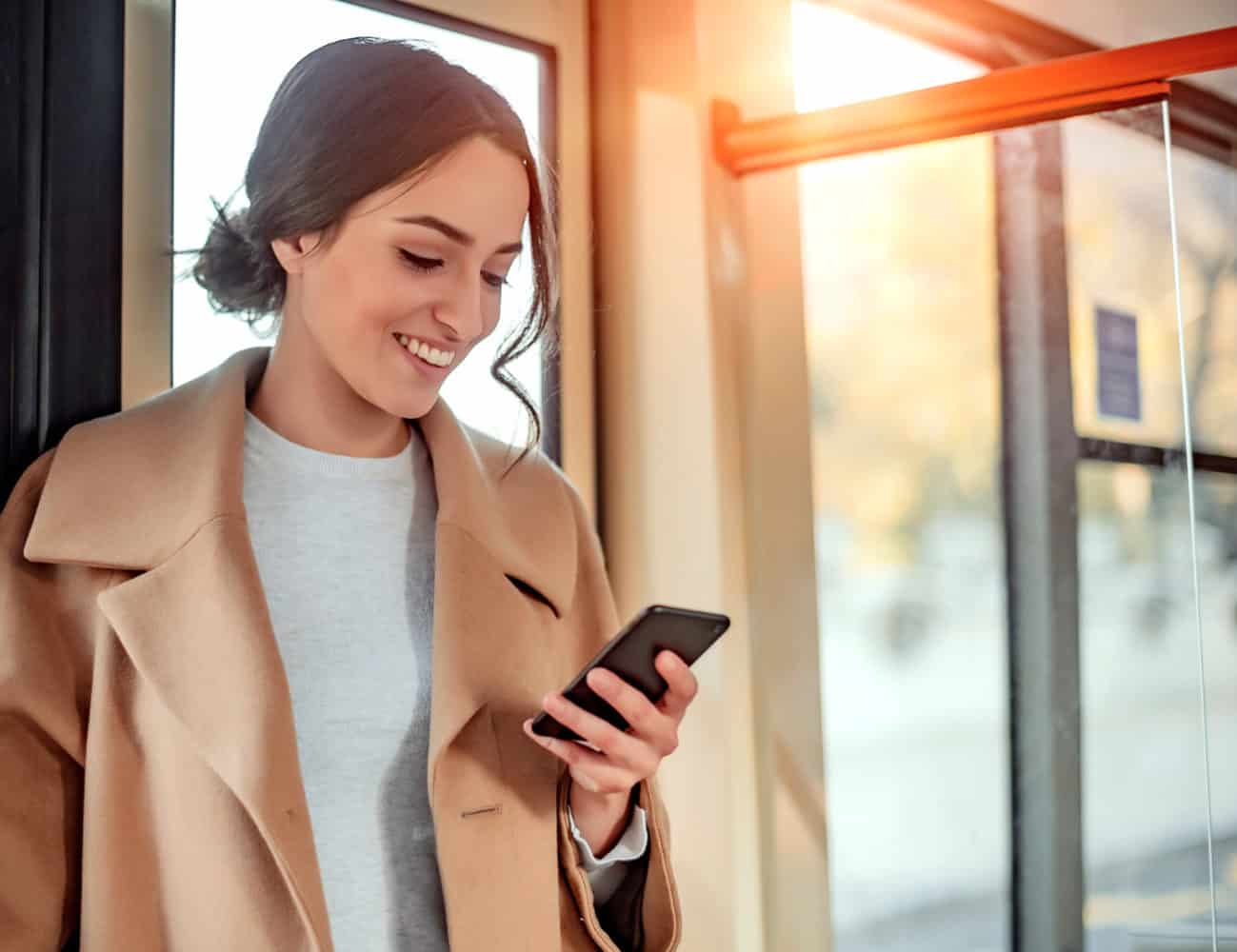 Woman in peach colored coat looking at her phone