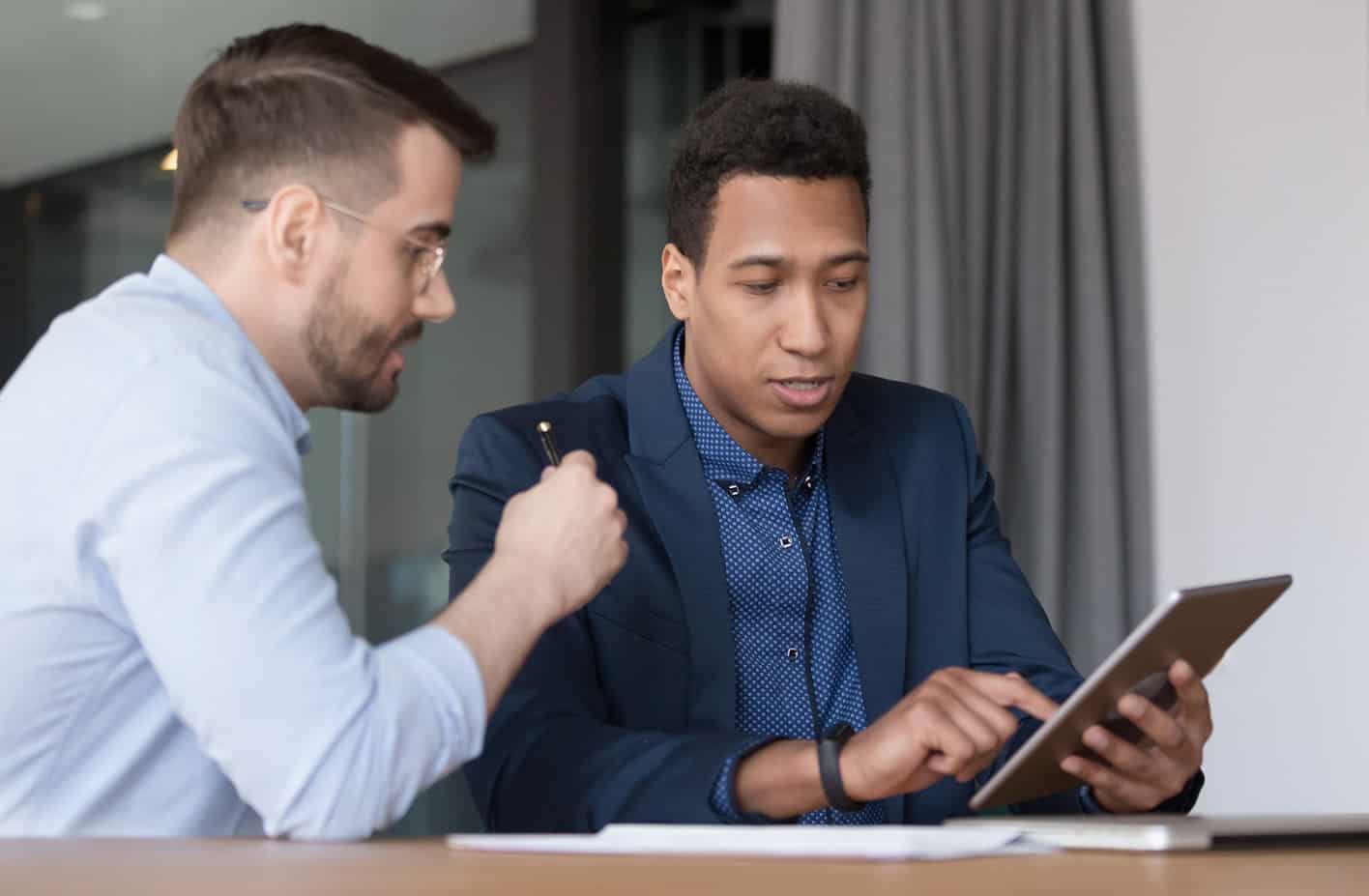 Two business men sitting at table looking at iPad