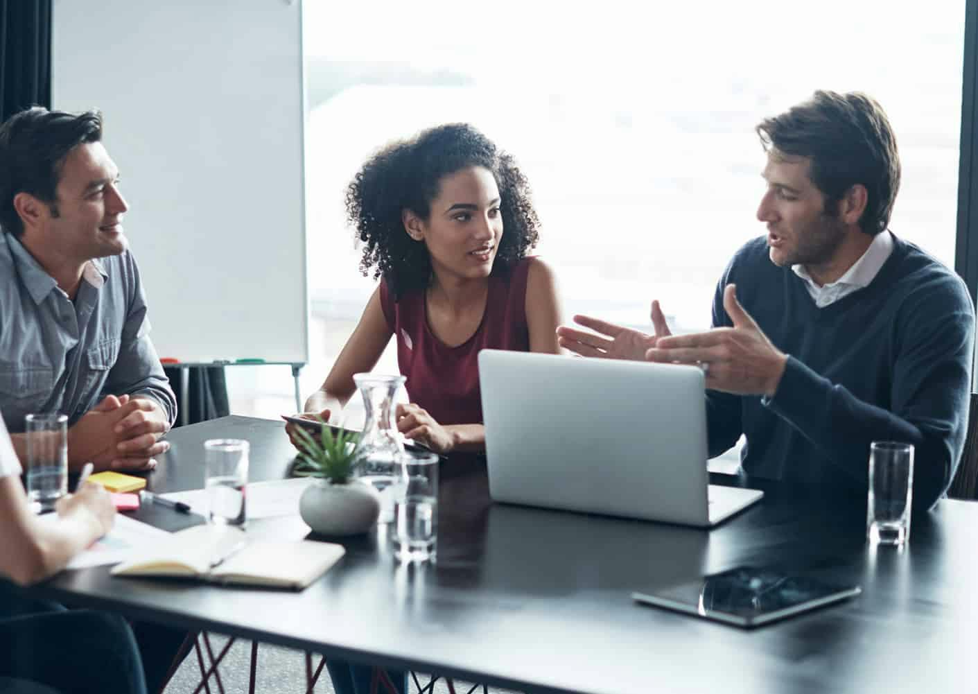 Group of people around a table talking with computers and paperwork
