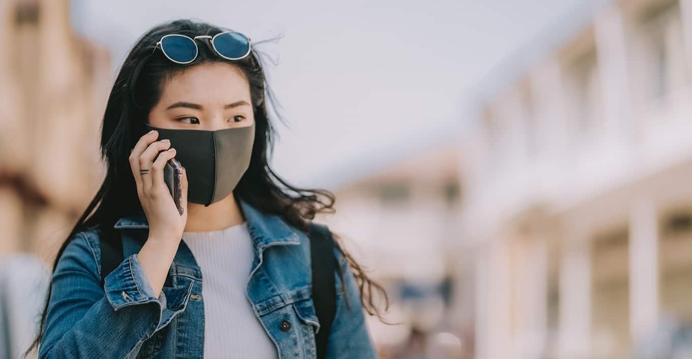 Woman walking outside talking on phone with mask on