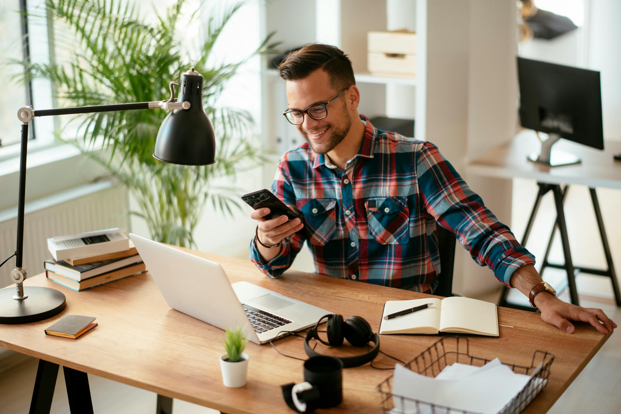 Smiling man sitting at a desk with a laptop and mobile phone