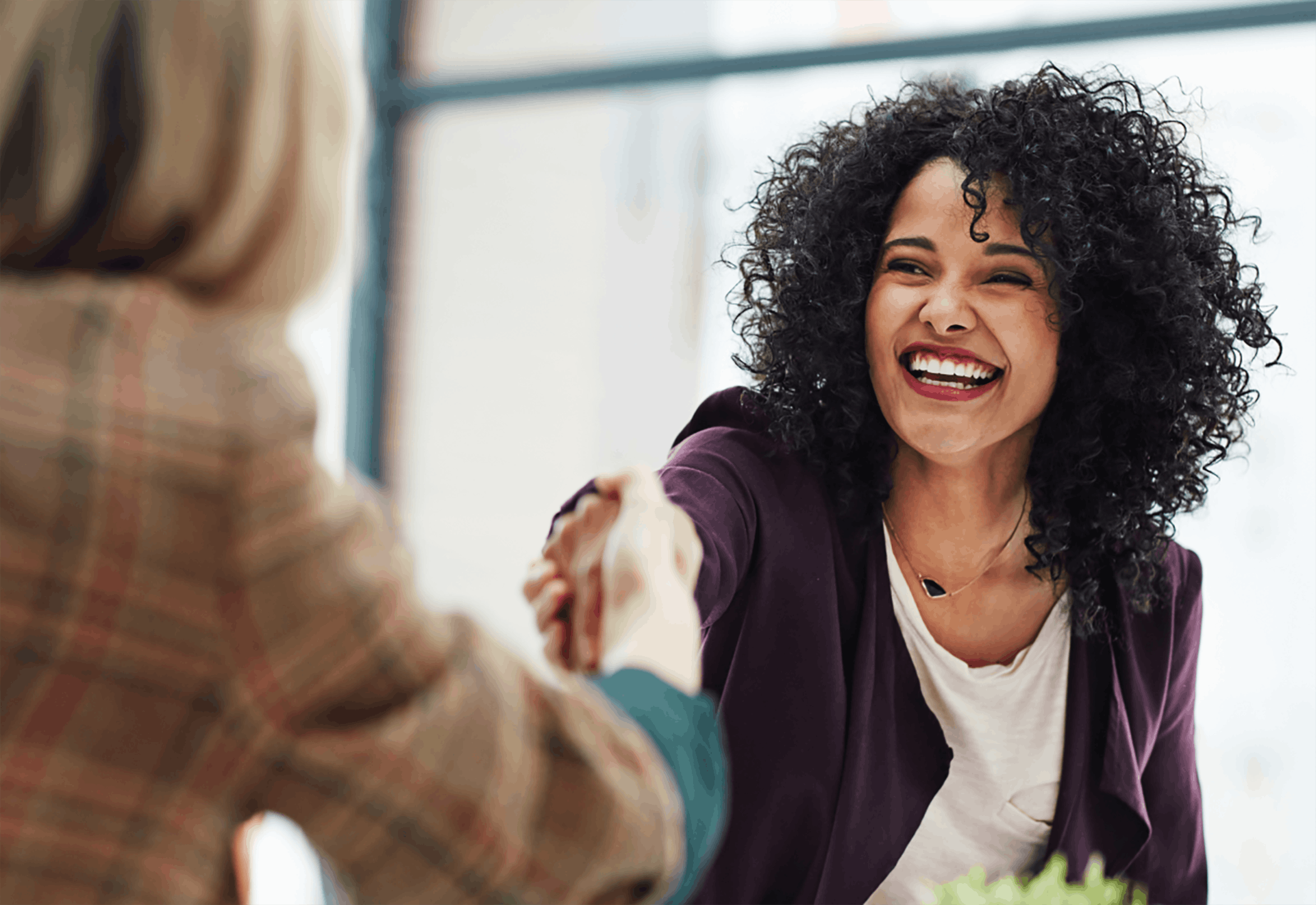 Two women shaking hands sitting at meeting