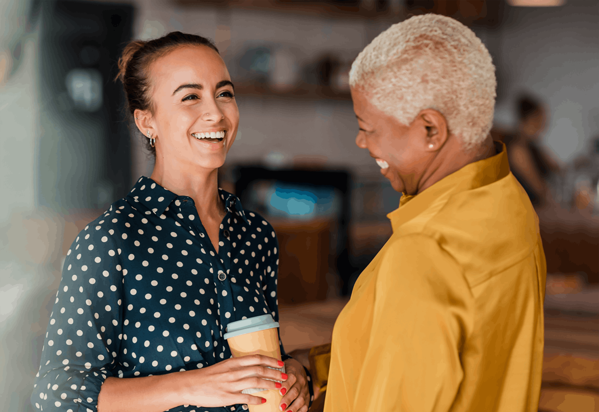 Two women talking holding coffee