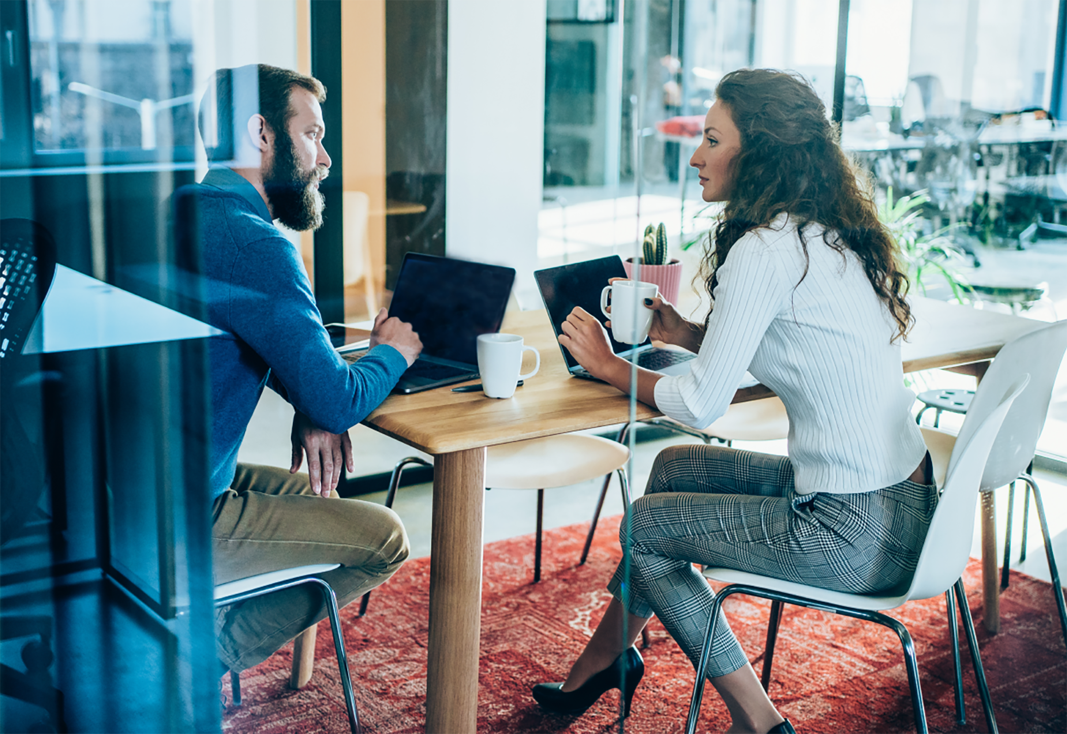 Woman and man sitting in conference room talking on laptops