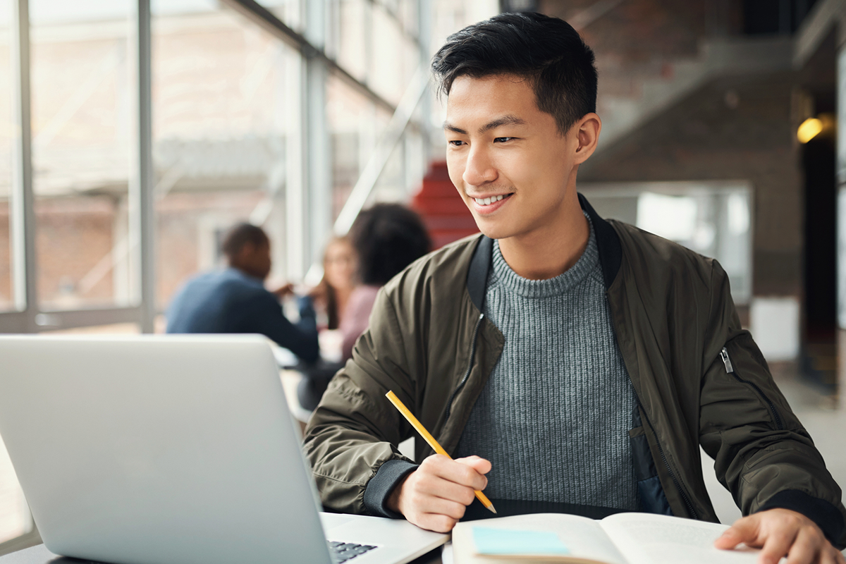 Young man looking at his laptop while taking notes